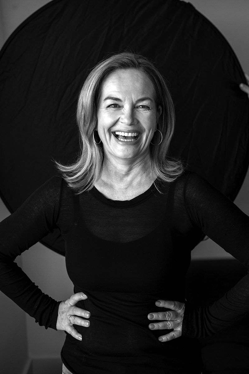 Black and white portrait of Claudia Mahler sitting on a sofa, wearing a white shirt, jeans, and glasses